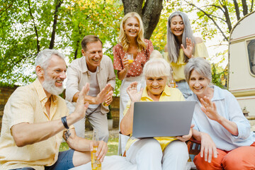 White friends laughing and using laptop during picnic on summer day