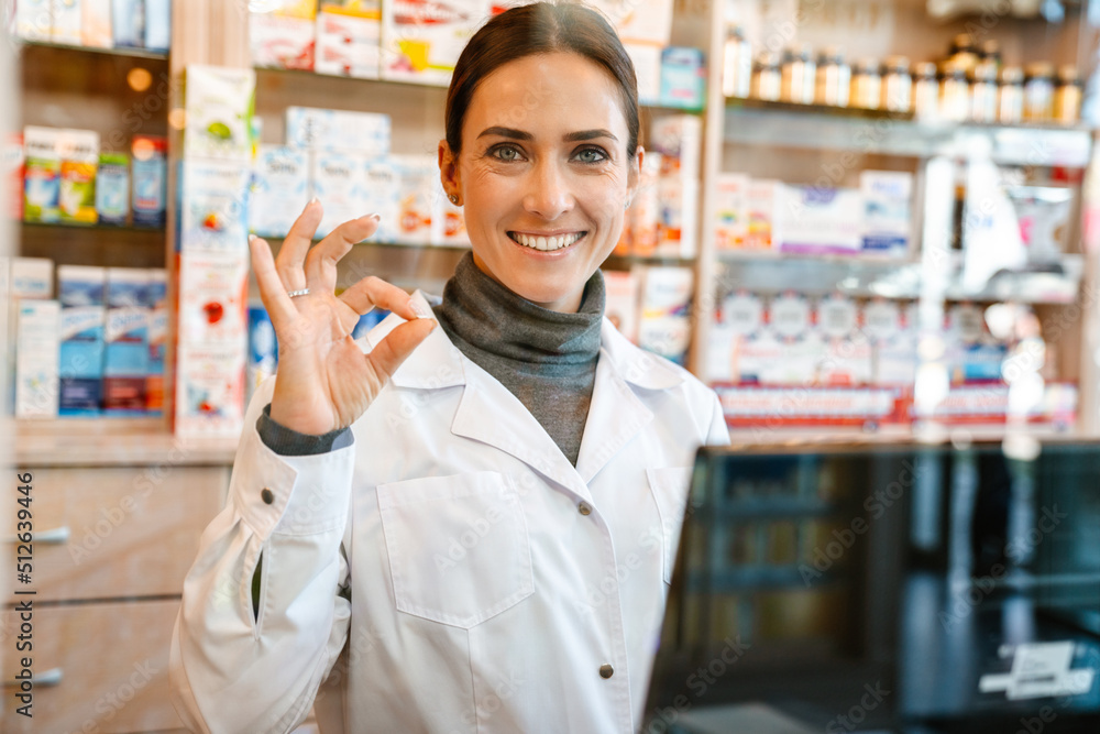 Wall mural White apothecary gesturing while working with till at pharmacy