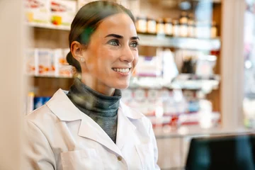 Zelfklevend Fotobehang White apothecary wearing lab coat smiling while working in pharmacy © Drobot Dean