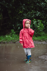 Beautiful girl walking along the puddles under the summer rain in a water-repellent raincoat and...
