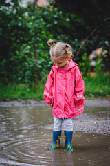 Beautiful girl walking along the puddles under the summer rain in a water-repellent raincoat and...