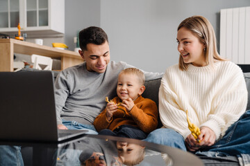 Happy white parents and little son using laptop on sofa at home