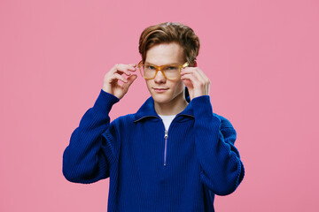 portrait of a guy adjusting his orange-rimmed glasses, standing in a blue sweater on a pink background