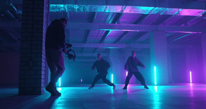 Back view of cameraman shooting video of dancers with electornic steadicam. Colorful neon light background. Slow motion. Backstage