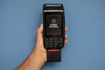 Credit or debit card terminal in hand isolated on blue background. Close up of POS terminal in hand processing a pay.