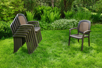 Stack of chairs in the garden. Plastic chairs in ornamental garden background. Selective focus.