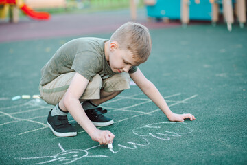 Kid boy draws painting a chalk on pavement asphalt on ground on playground. Creative children...