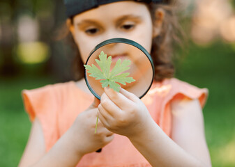 Caucasian little cute girl exploring nature environment with a magnifying glass loupe