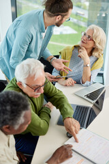 Obraz premium Young hipster educator teaching a multicultural group of senior students how to use the internet in the classroom.