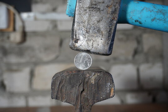 A one-ruble coin between a hammer and an anvil, against a brick wall. Strong ruble