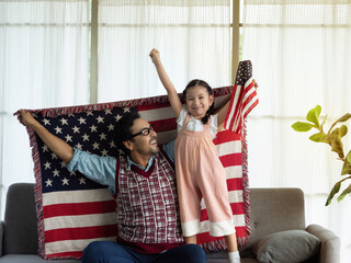 Happy family, close up single father and cute little daughter sitting on sofa at home with flags of United States of America, celebrating independence Day. 4th of July, Patriotic US holiday,