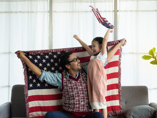 Happy family, Single father and cute little daughter sitting on sofa at home with flags of United States of America, celebrating independence Day. 4th of July, Patriotic US holiday,