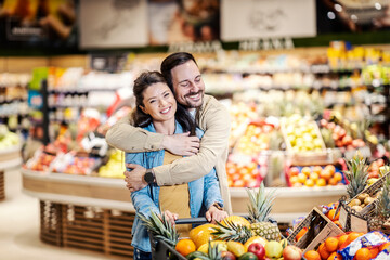 A couple in love hugging in supermarket while purchasing in supermarket.