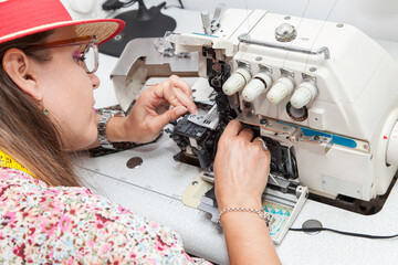 beautiful stylish woman designer inserts thread into overlock machine.