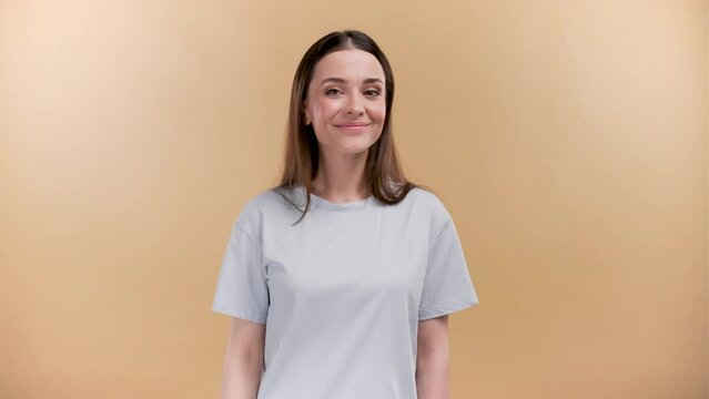 Cheerful young caucasian woman in white t-shirt isolated on beige background. Doing phone gesture says call me back smiling looking at the camera.