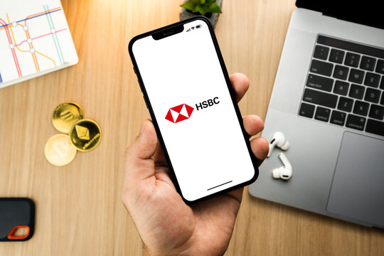 Man holding a smartphone with HSBC bank app on the screen on wooden table with a cryptocurrencies coins and computer. Office environment. Rio de Janeiro, RJ, Brazil. June 2022