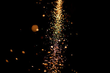 Sparks in dark. Flow of sparks from metal processing. Lights on black background. Work in workshop. Grinding steel. Many small particles burn brightly.