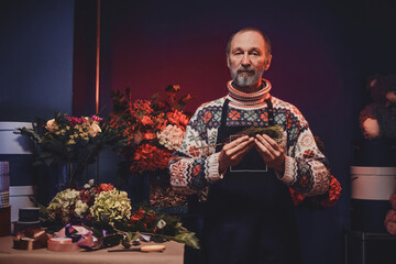 Portrait of senior man florist and his workpalce there are colorful flowers and table.