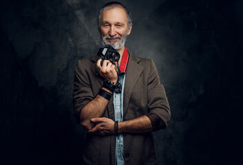 Portrait of senior man photographer with beard holding digital camera against dark background.
