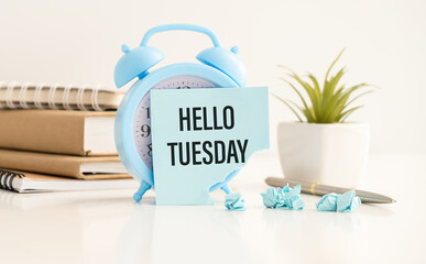HELLO TUESDAY, text on sticky paper on an alarm clock with a pen and glasses, light background