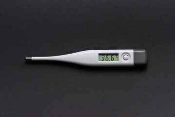 white electronic thermometer shows normal body temperature on a black background
