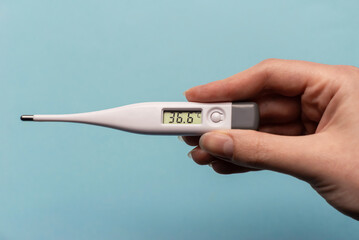 woman hand holding thermometer on a blue background. thermometer shows normal temperature.