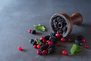 Ceramic bowl full of tobacco for hookah, scattered mulberry and cranberry on the grey background. Copy space