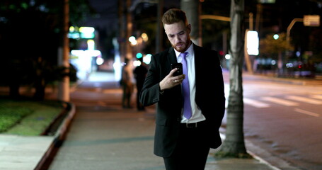 Business man looking at cellphone device at night walking on sidewalk