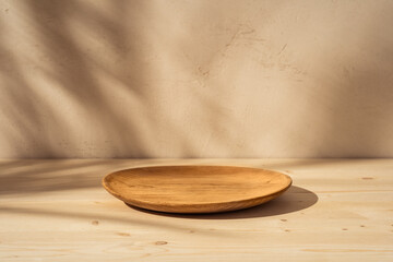 Wooden plate or bowl on wooden table on stucco background with branch shadow on the wall. Mock up...