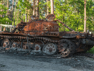 Fototapeta na wymiar War in Ukraine, a destroyed Russian tank with a Ukrainian ensign stands near the road against the backdrop of the forest, side view 