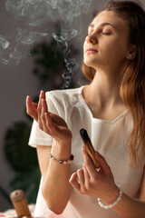 A young woman holds a smoking palo santo stick in her hands.Alternative medicine.Clearing the space...