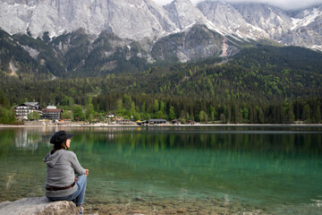 Caucasian female sitting on a stone near the Eibsee Lake, Germany. Travel, lifestyle concept.
