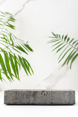 Concrete black podium for cosmetic products close-up among tropical leaves on the background of a marble white wall