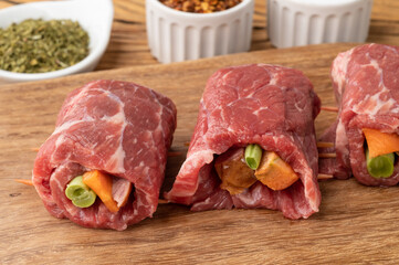 Rolled beef or roulade, vegetable and bacon stuffed meat over wooden table with seasonings
