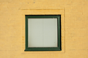 Green window with blinds on yellow plastered old wall