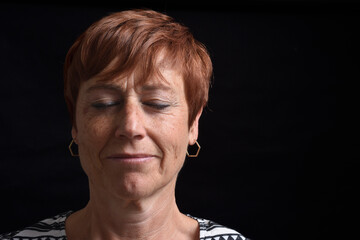 middle aged woman with eyes clossed on black background