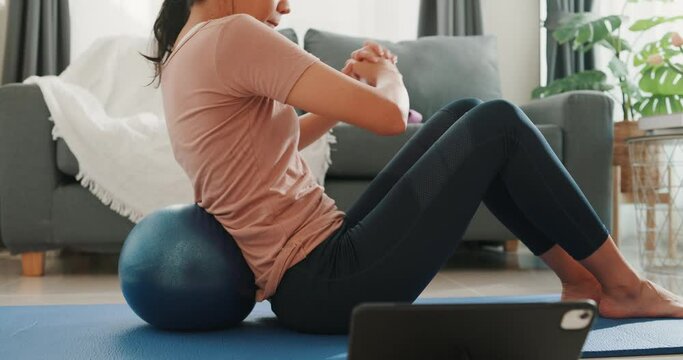 Close up of Young attractive Asia woman in sportswear watching fitness online video on tablet with fitness ball in living room at house. Home quarantine workout and fitness exercise without the gym.