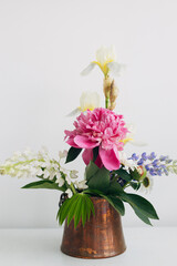 Modern summer flowers still life arrangement in vintage vase on white wood. Creative floral image. Stylish peony, lupin, iris and daisy composition on rustic table