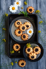 vertical composition. Homemade cookies and chamomile flowers on metal bowls and a tray on a gray background. View from above