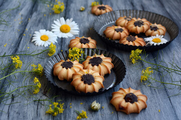Patterned shaped cookies on metal bowls and chamomile flowers on a rustic gray background
