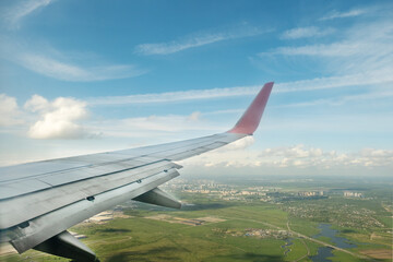 Wing of the plane, landscape below and clouds in porthole. Flight on vacation, on weekends. Travel...