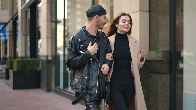 Relaxed cheerful gay man and young woman talking strolling on city street arm in arm. Dolly shot portrait of positive Caucasian friends gossiping walking outdoors leaving