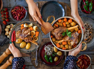 Cooked shank with vegetables in the cooking pot. Many foods on the table. 