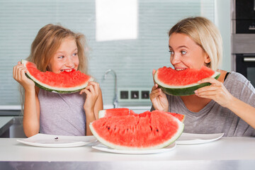 Mother and child daughter are eating watermelon at home