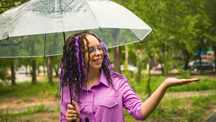 A woman with umbrella in hand in the rain. Girl with glasses under an umbrella against the backdrop...