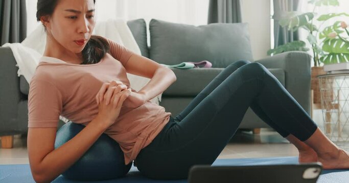 Close up of Young attractive Asia woman in sportswear watching fitness online video on tablet with fitness ball in living room at house. Home quarantine workout and fitness exercise without the gym.