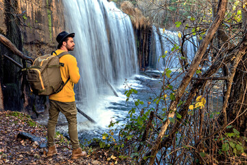 young backpacker looking at the waterfall in the forest