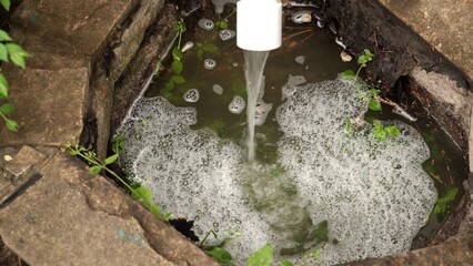 Dirty, foamy, wastewater flows out of pipe.
