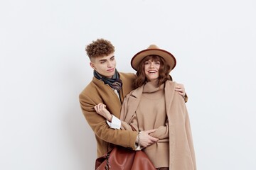 a beautiful, loving couple of a man and a woman stand on a white background in stylish autumn clothes, gently embracing and the woman happily looks at the camera, and the man at her