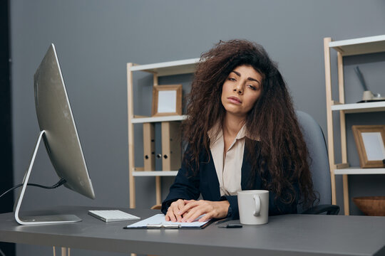 Tired Bored Sleepy Tanned Adorable Curly Latin Businesswoman In Jacket Have Too Much Work Looks At Camera In Office. Copy Space Mockup Banner. Corporation Leader Lady Uses Modern Computer In Work